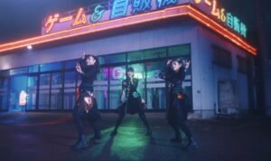 Babymetal members dancing in front of neon sign building